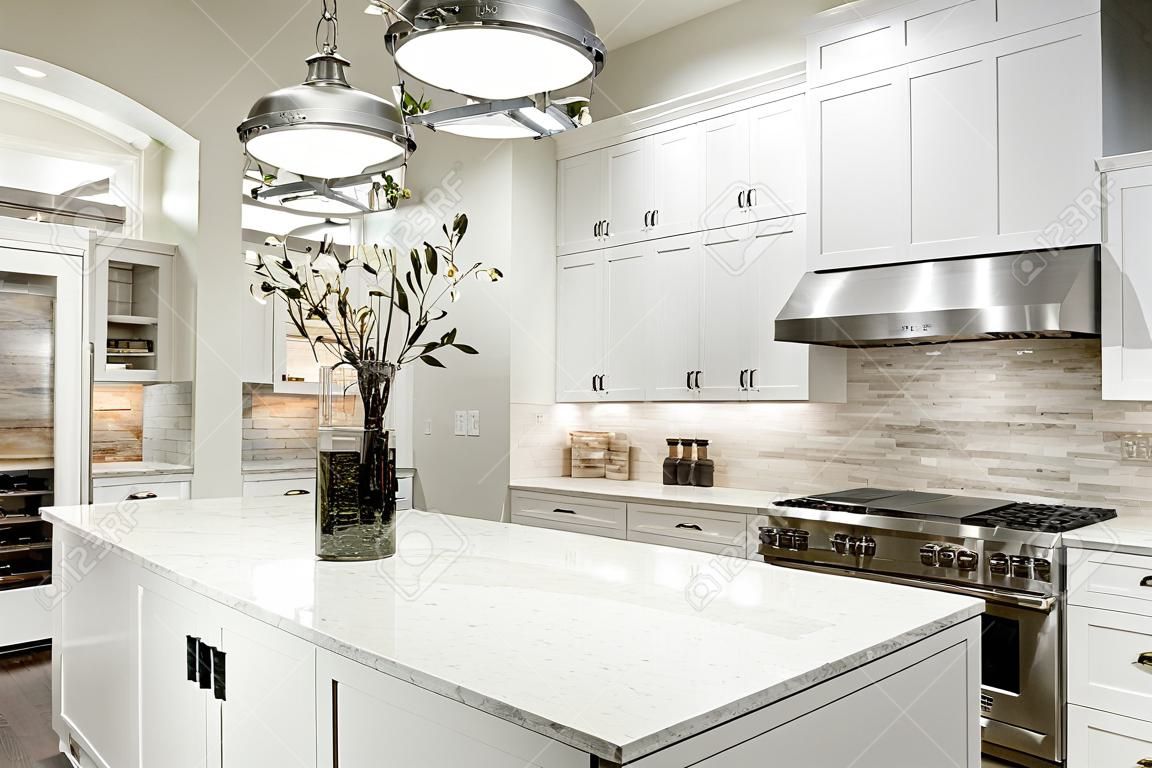 Cozinha gourmet apresenta armários shaker branco com bancadas de mármore, pedra backsplash de telha do metrô, porta dupla geladeira de aço inoxidável e linda ilha de cozinha.