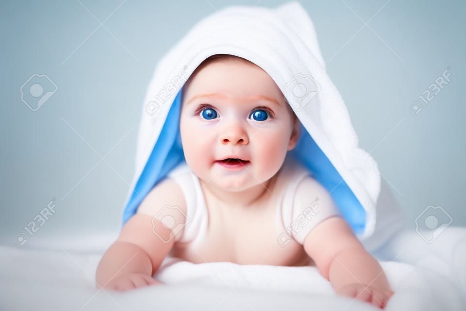 Şirin bebek kızı veya oğlan duştan sonra beyaz güneşli yatak odasında baş havluyla. Büyük mavi gözlü çocuk, yataktan banyodan sonra rahatlarken