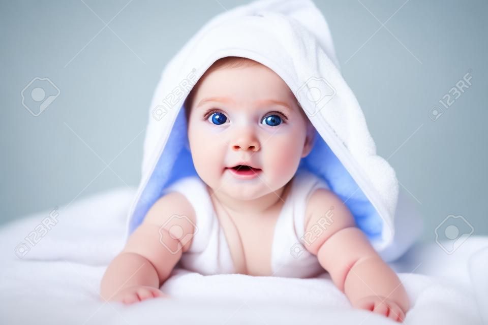 Bambina o ragazzo sveglio dopo la doccia con il tovagliolo sulla testa nella stanza bianca soleggiata. Bambino con grandi occhi blu rilassante a letto dopo il bagno