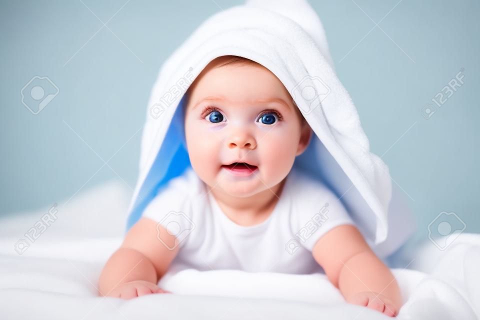 Şirin bebek kızı veya oğlan duştan sonra beyaz güneşli yatak odasında baş havluyla. Büyük mavi gözlü çocuk, yataktan banyodan sonra rahatlarken