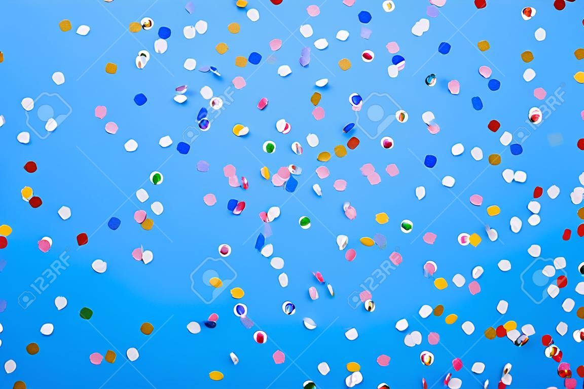 Kolorowe konfetti rozrzucone na niebieskim papierze pastelowym
