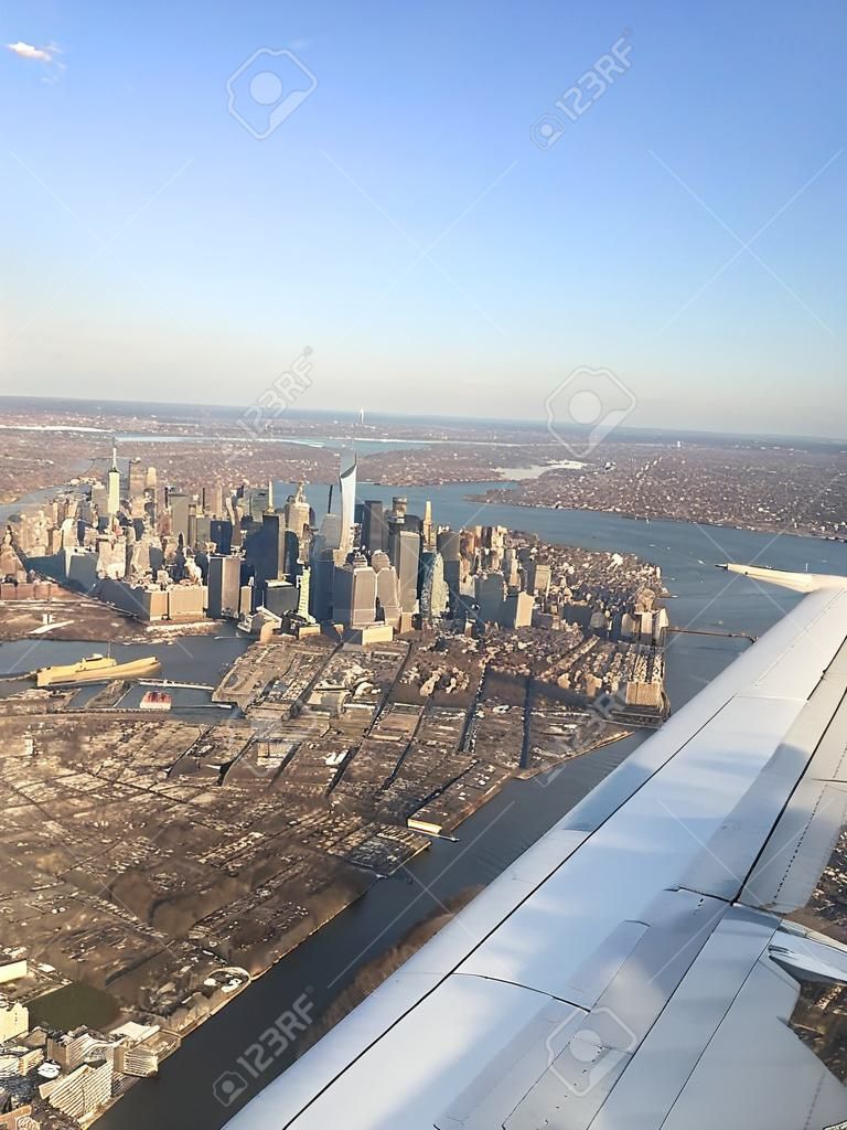 Vertical aerial view from an airplane wing of New Jersey landmarks & the urban downtown Manhattan metropolis' buildings & cityscape (New York City in the United States of America) in the background