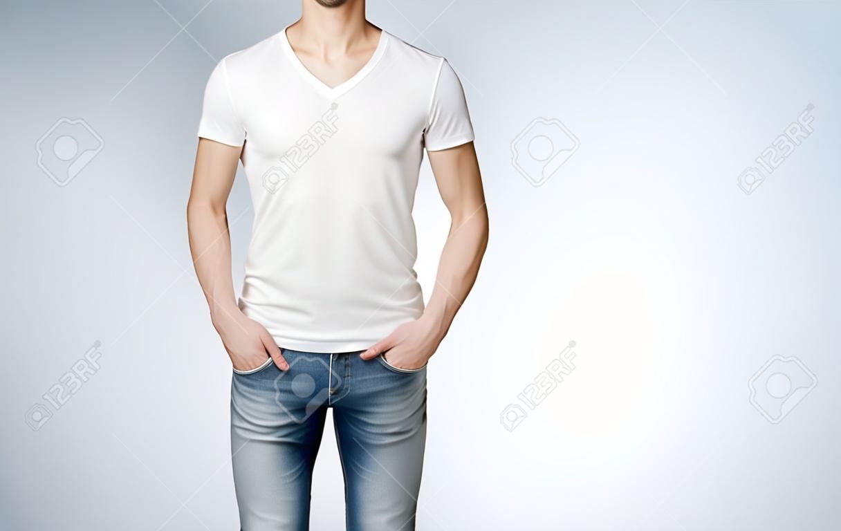 Man in a white T-shirt and jeans with hands in pockets, no face. Grey background. Front view. Concept of casual clothes.