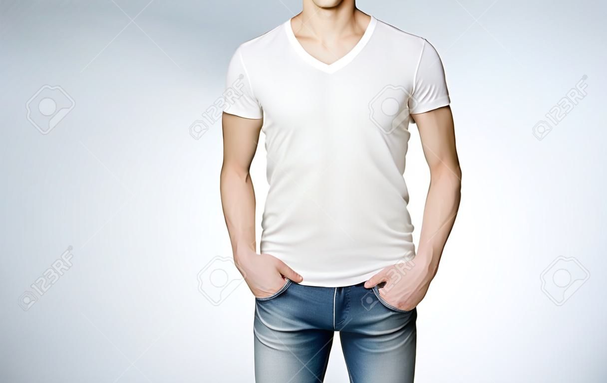 Man in a white T-shirt and jeans with hands in pockets, no face. Grey background. Front view. Concept of casual clothes.