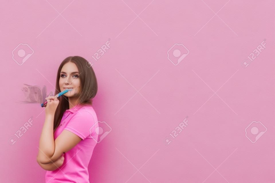 Portrait of young caucasian woman with long fair hair wearing pink polo shirt, holding marker and thinking standing near gray wall. Concept of planning. Mock up