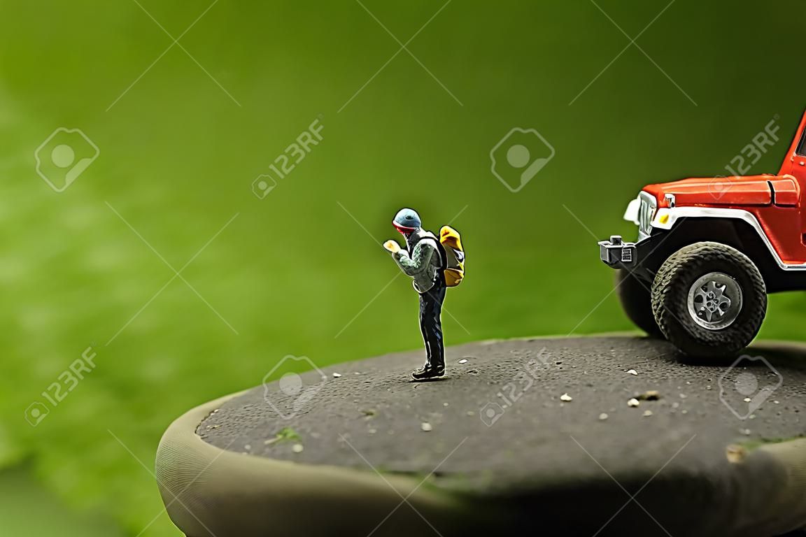 Miniature backpacker standing on rock with green background
