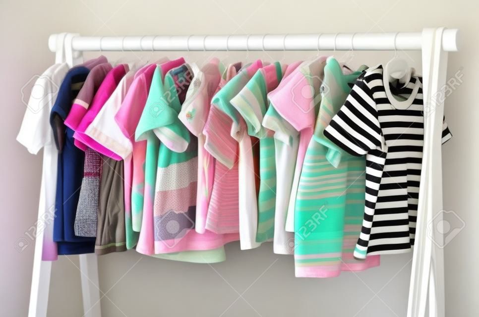 Dressing closet with clothes arranged on hangers.Colorful wardrobe of newborn,kids, toddlers, babies full of all clothes.Many t-shirts,pants, shirts,blouses, onesie hanging