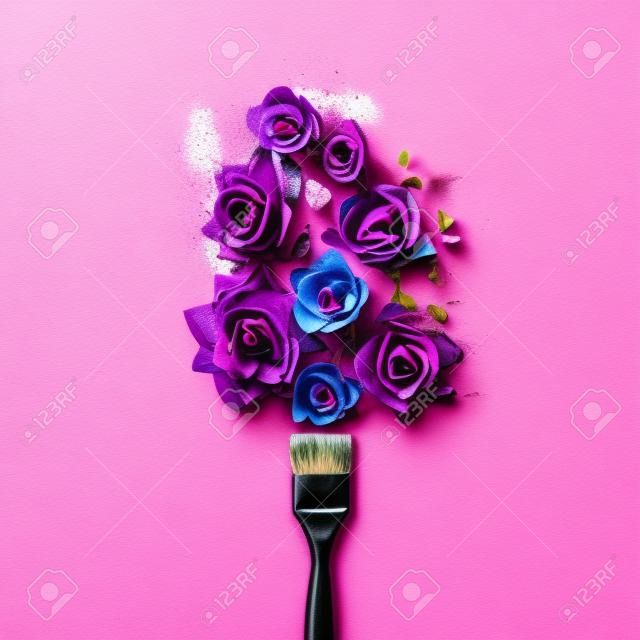 Purple flowers and paint brush on pink background. Flat lay.