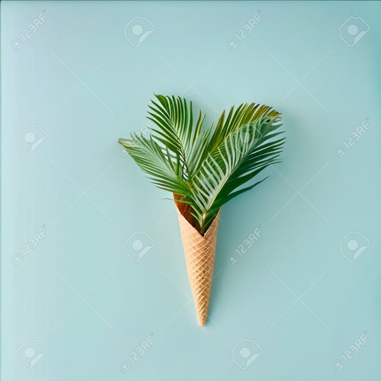 Palm tree leaves in ice cream cone on pastel blue background. Flat lay. Summer tropical concept.