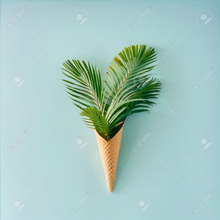 棕櫚樹在粉紅色的藍色背景上的冰淇淋錐。平躺。夏季熱帶概念。