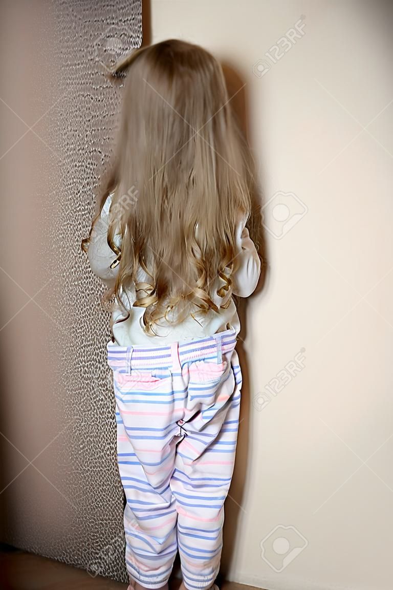 Непослушный маленькая девочка стоит в углу наказывали у себя дома