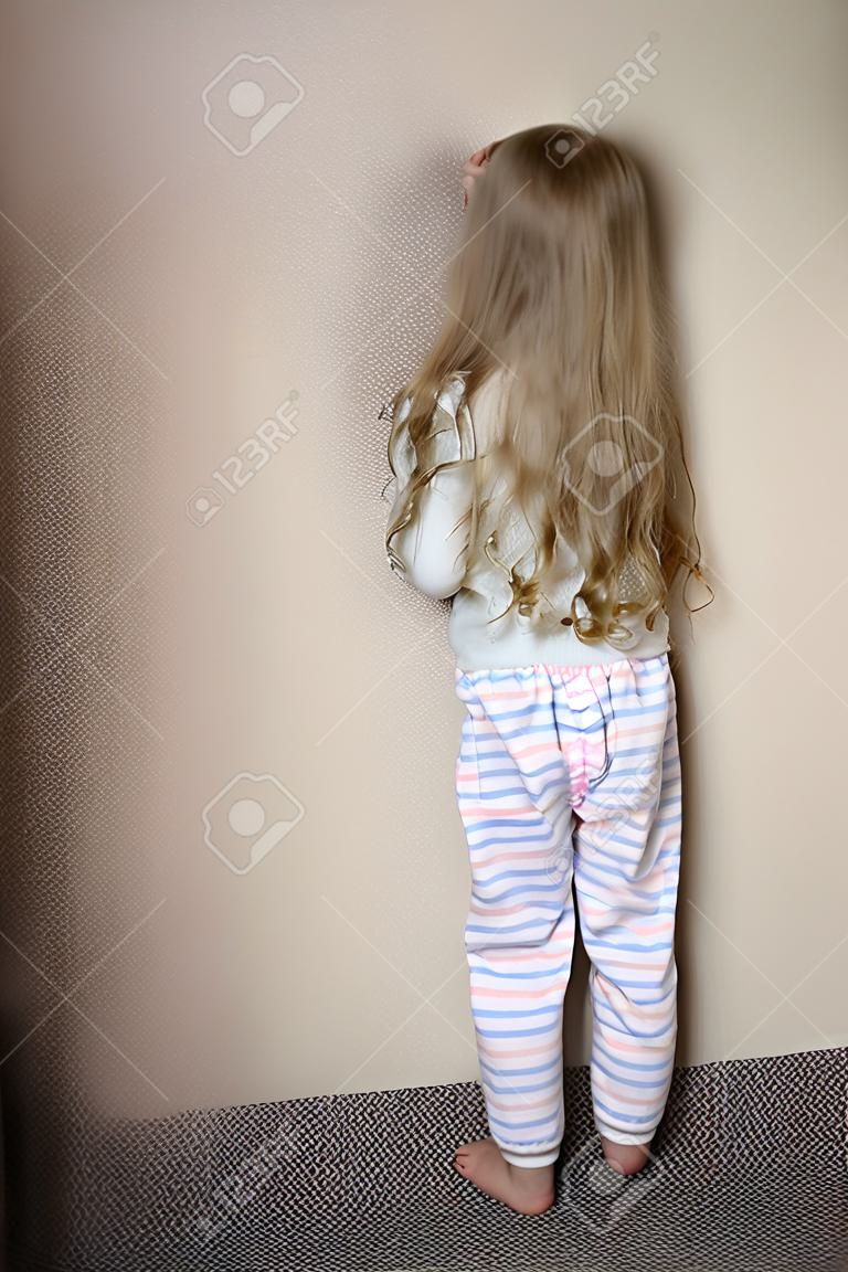 Freches kleines Mädchen in der Ecke zu Hause bestraft stehend