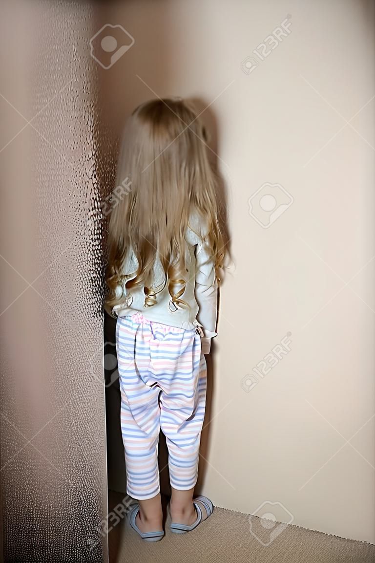 Непослушный маленькая девочка стоит в углу наказывали у себя дома