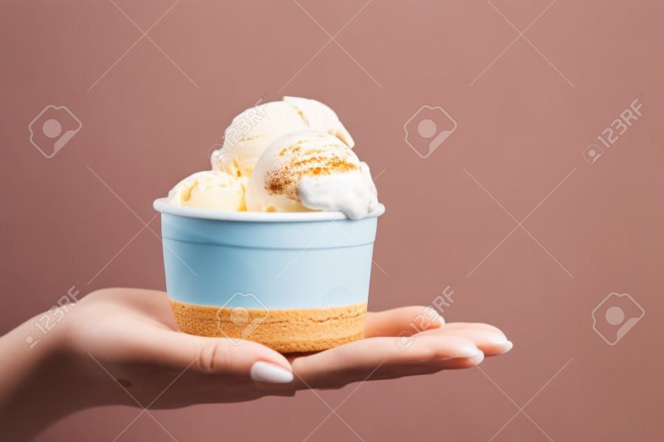 ragazza che tiene una tazza piena di gelato nel palmo della mano. Foto di concetto del venditore. Il concetto di fotografia di cibo.