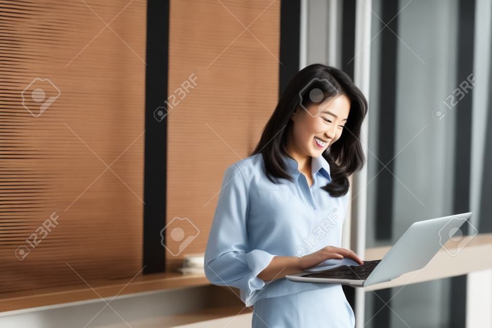 Happy attractive asian business woman  smiling working with laptop in modern office