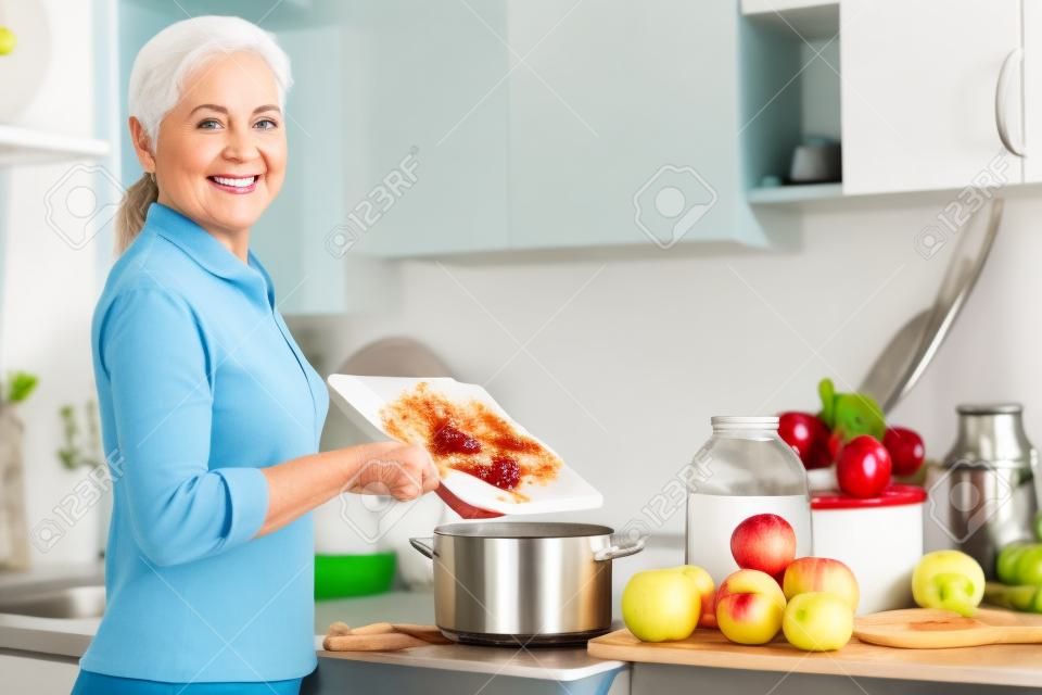 Érett nő főz almaszósz jam a konyhában