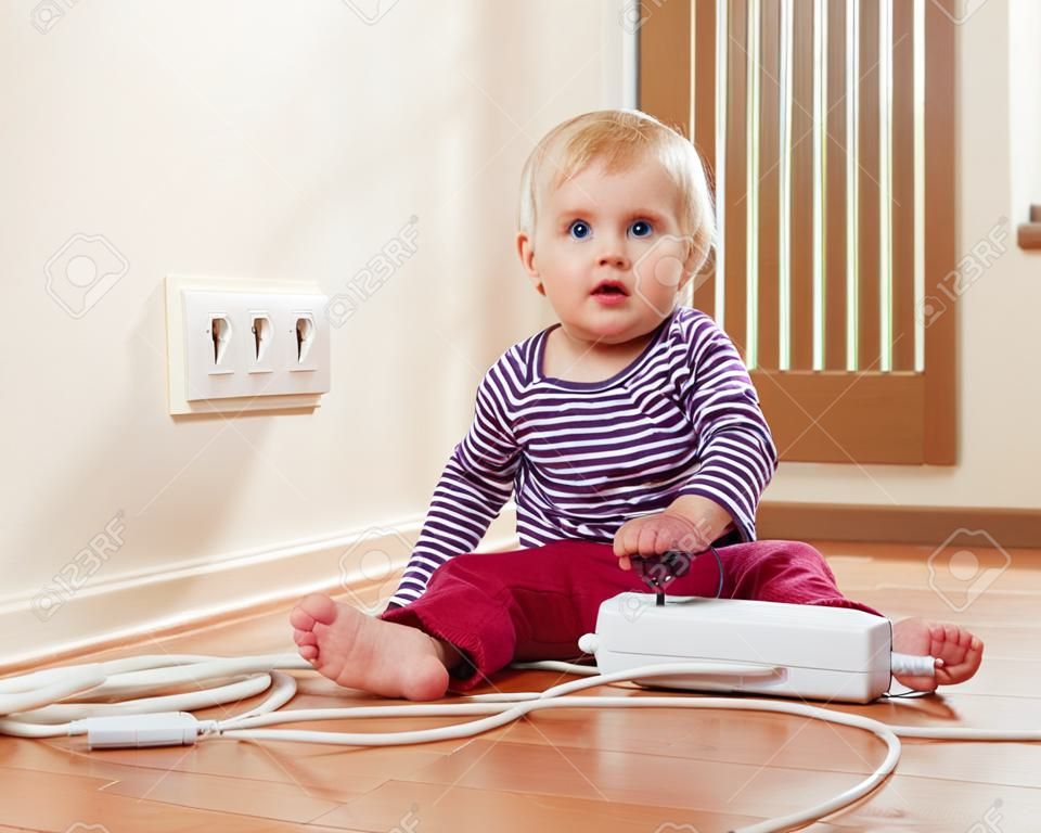 Bebé que juega con la extensión eléctrica y toma de corriente de baja