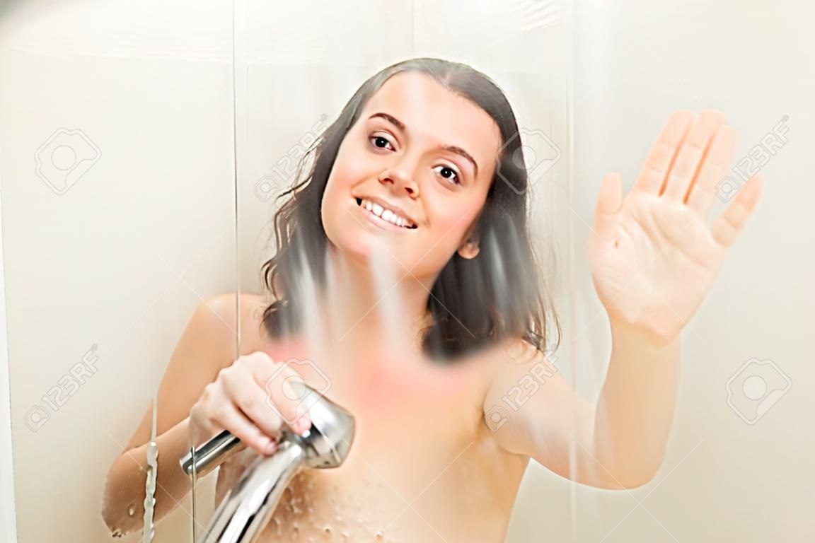 Uśmiechnięta dziewczyna relaksująca się za płaczącą szybą kabiny prysznicowej