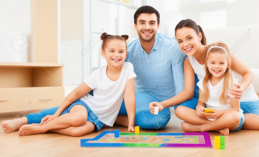 Sonriendo familia joven con dos niños jugando al juego de mesa en el interior doméstico