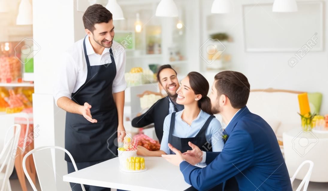 Smiling couple guests giving order to welcoming waiter in confectionery
