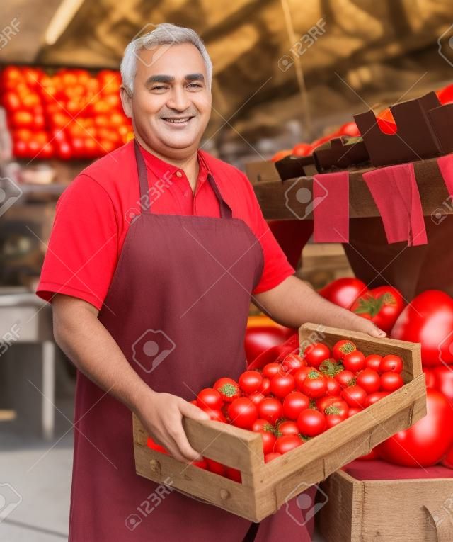 el vendedor adulto está ofreciendo tomates rojos en el mercado.