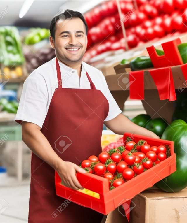 dorosły sprzedawca oferuje na rynku czerwone pomidory.