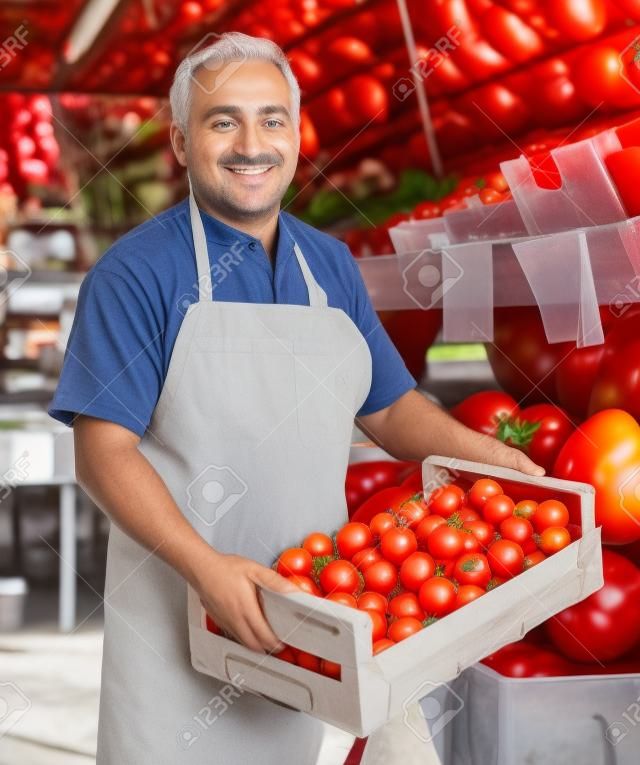 dorosły sprzedawca oferuje na rynku czerwone pomidory.