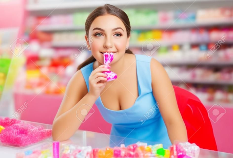 Young girl posing in the store with lolly on the background of counters with sweets