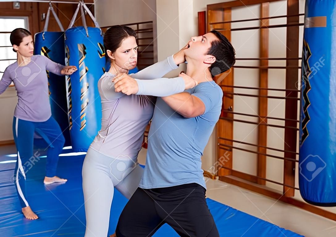 Adult people practicing effective techniques of self-defence in training room