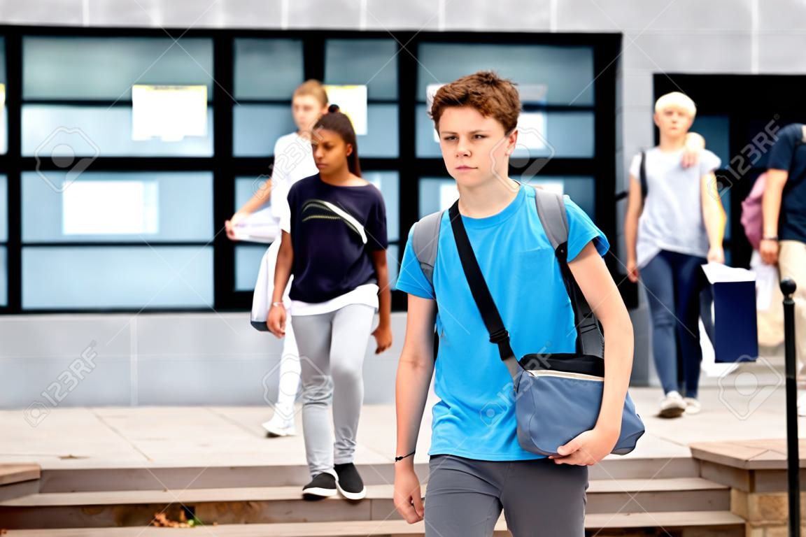 Positive teenager walking in the street carrying bag on one shoulder