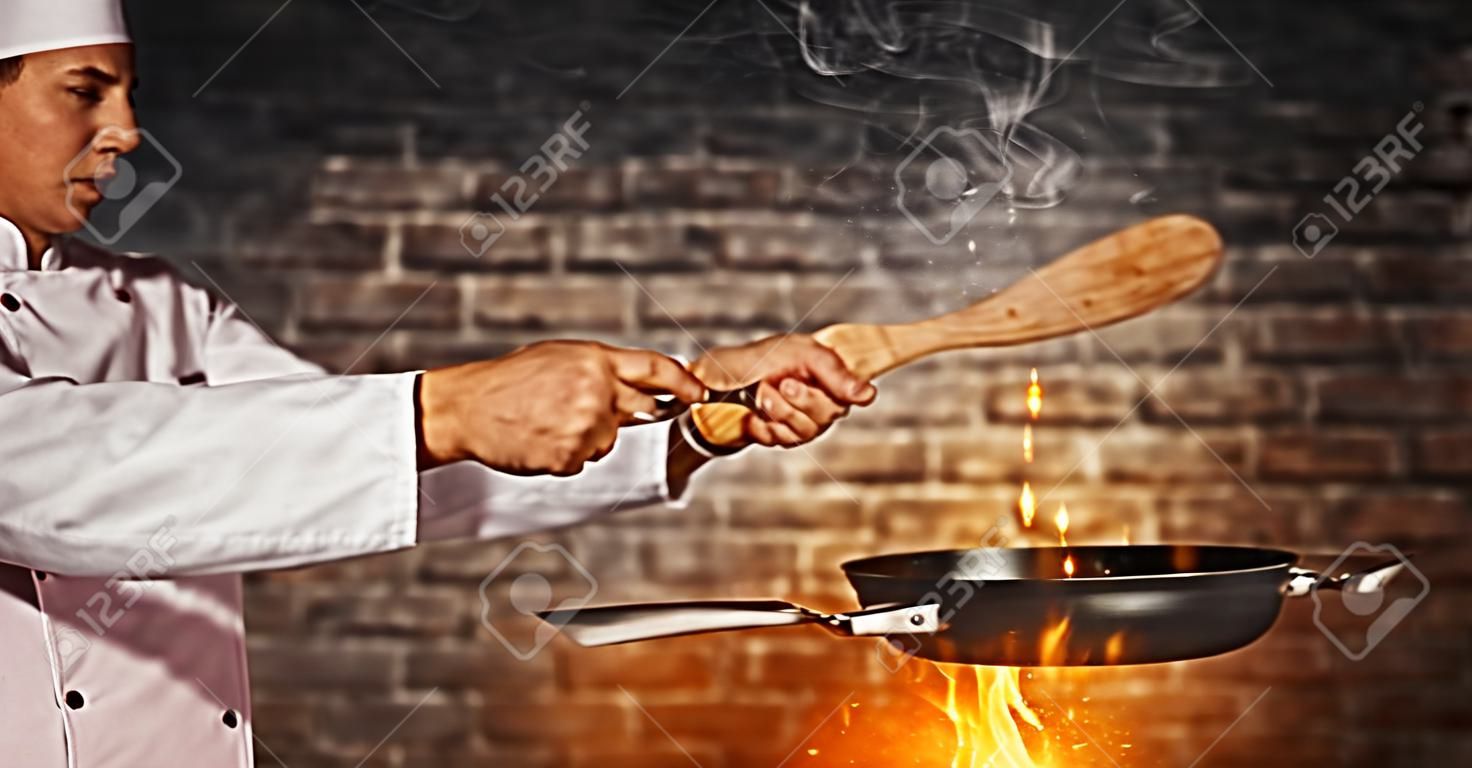Zbliżenie kuchenka szefa kuchni gotowa do gotowania, trzymając pustą patelnię grillową, latający efekt ruchu gotowy do umieszczenia produktu stary ceglany mur na tle