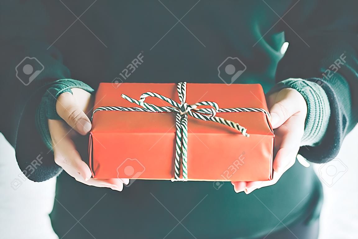 Woman hands holding Christmas handmade gift box or new year present with snow background. vintage color tone