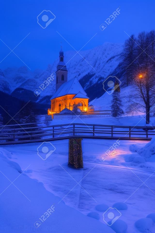 Schöne Dämmerungsansicht der Sankt Sebastian-Wallfahrtskirche mit dem verzierten Weihnachtsbaum belichtet während der blauen Stunde an der Dämmerung im Winter, Ramsau, Nationalpark Berchtesgadener Land, Bayern, Deutschland