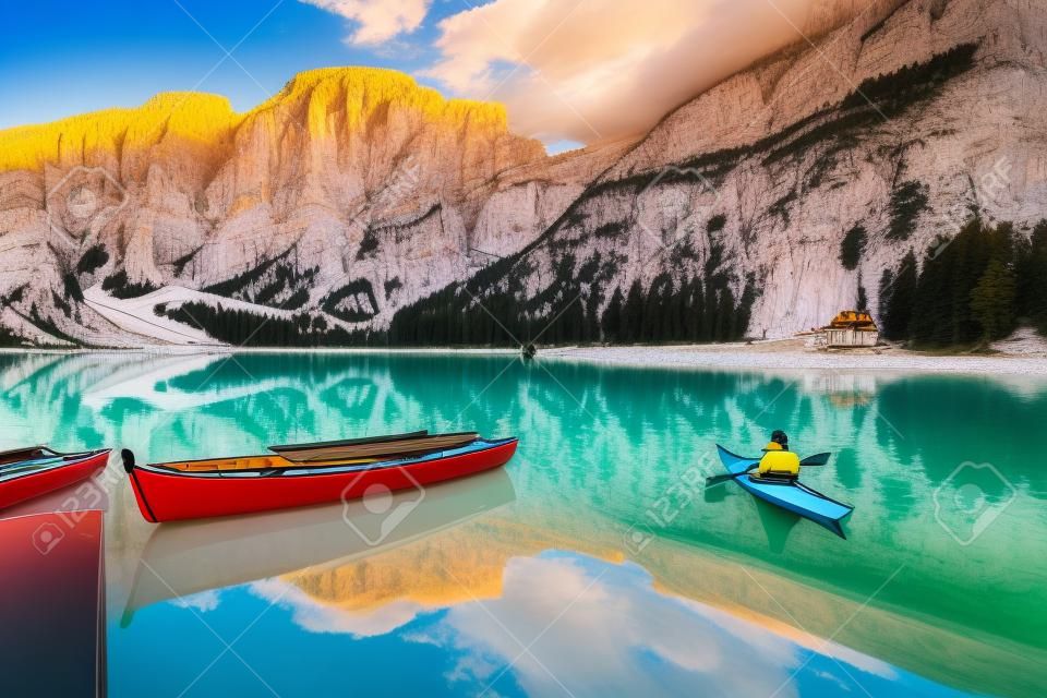 Beautiful view of famous Lago di Braies with traditonal rowing boat and young man in kayak at sunrise in fall, Dolomites, Italy