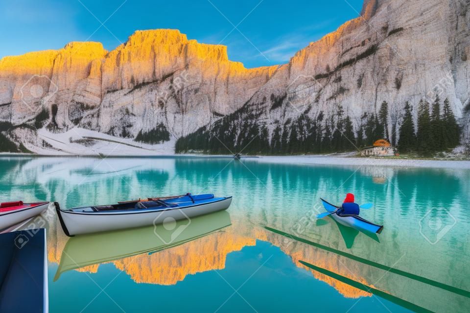 Beautiful view of famous Lago di Braies with traditonal rowing boat and young man in kayak at sunrise in fall, Dolomites, Italy