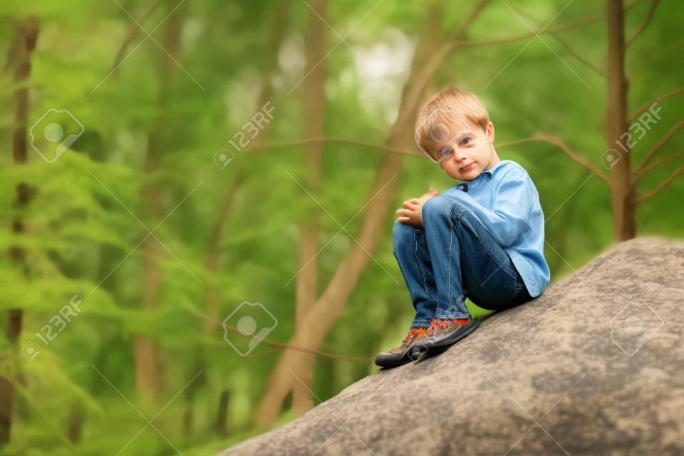 Un petit garçon s'asseyant sur grand bouder de roche.