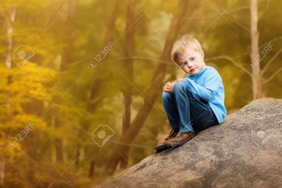 Un petit garçon s'asseyant sur grand bouder de roche.