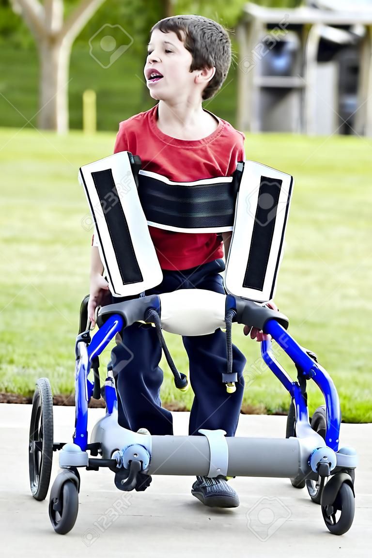 五歲的殘疾人男孩在學步車由公園。他有腦性麻痺。