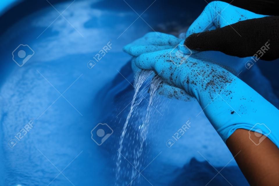 Mãos da mulher que lavam a roupa preta na bacia azul