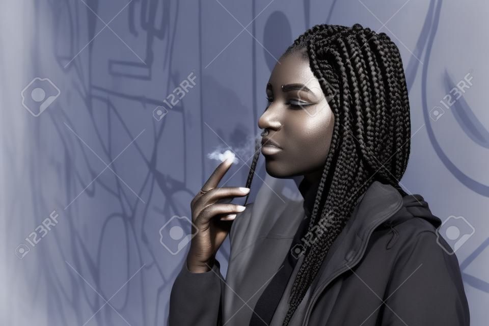 Geflochtene junge Frau raucht im Freien. Mit afrikanischen Zöpfen, durchbohrte Mode Frau. Umwandlung in Schwarz und Weiß, Getreide hinzugefügt.