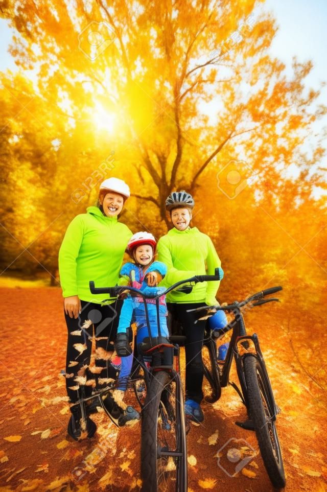 Familia en las bicis en parque del otoño, los padres y el niño en bicicleta, deporte familiar activo al aire libre, imagen vertical
