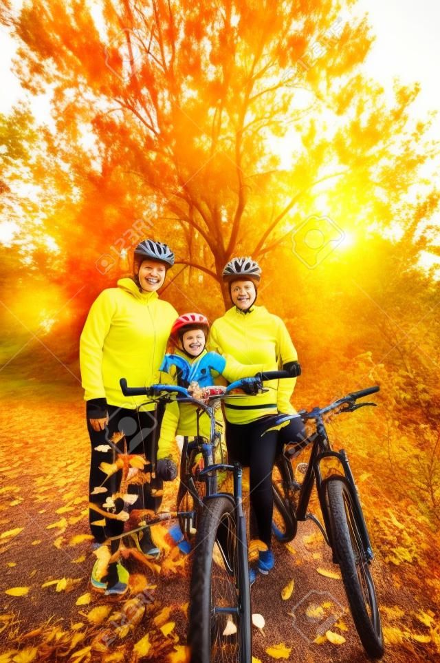 Familia en las bicis en parque del otoño, los padres y el niño en bicicleta, deporte familiar activo al aire libre, imagen vertical