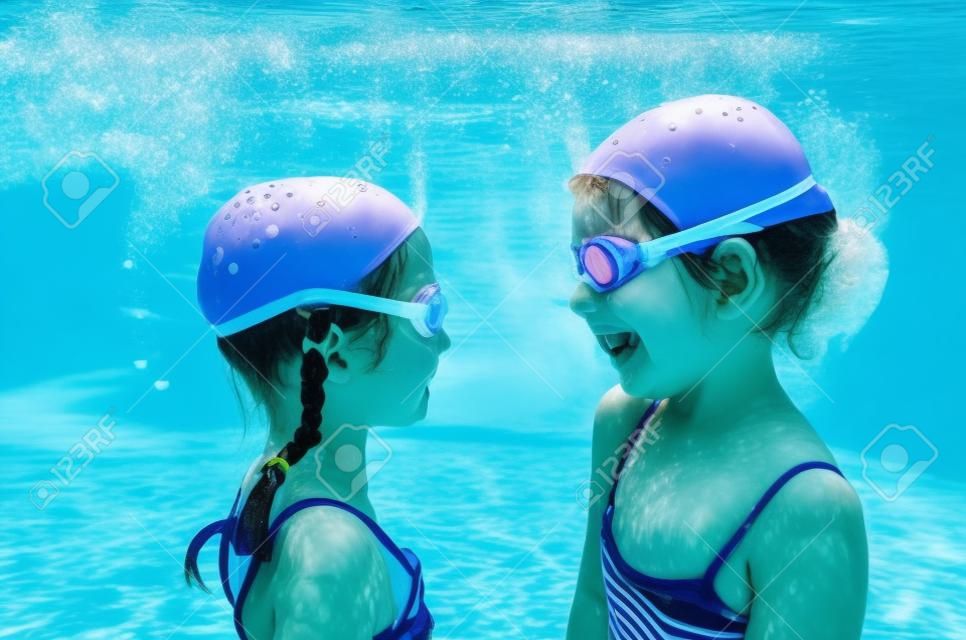 Children swim underwater in swimming pool, happy active girls have fun under water, kids fitness and sport on active family vacation