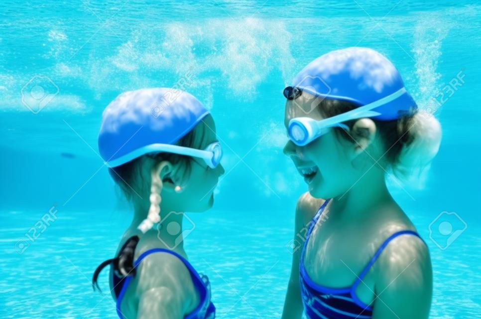Children swim underwater in swimming pool, happy active girls have fun under water, kids fitness and sport on active family vacation