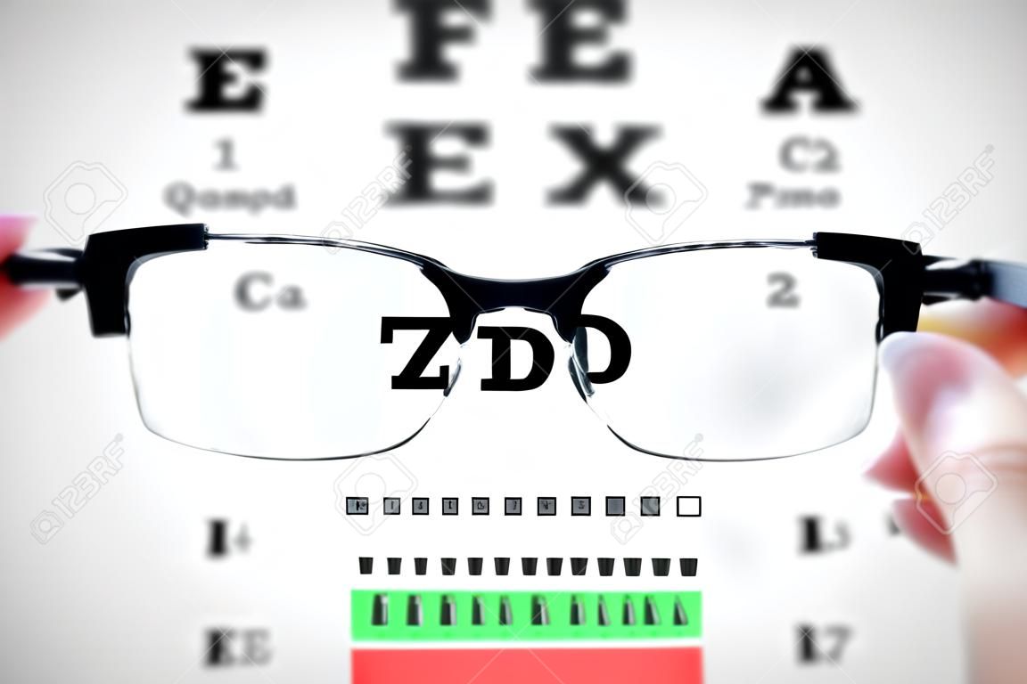 視力テスト グラフ基板上でメガネを保持している女性の手。
