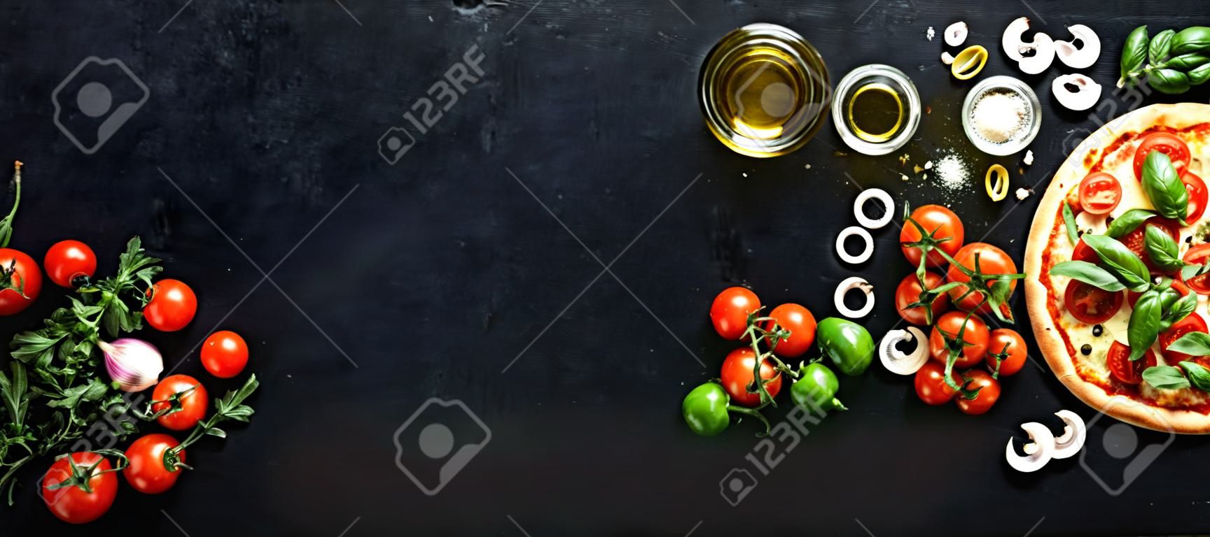 Food ingredients and spices for cooking mushrooms, tomatoes, cheese, onion, oil, pepper, salt, basil, olive and delicious italian pizza on black concrete background. Copyspace. Top view. Banner