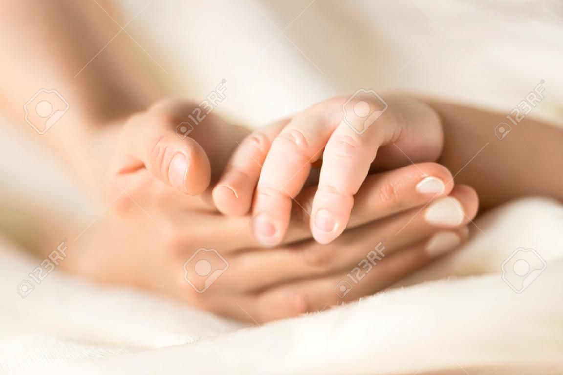 Main féminine tenant la main de son nouveau-né. Maman avec son enfant. Maternité, famille, concept de naissance. Copiez l'espace pour votre texte