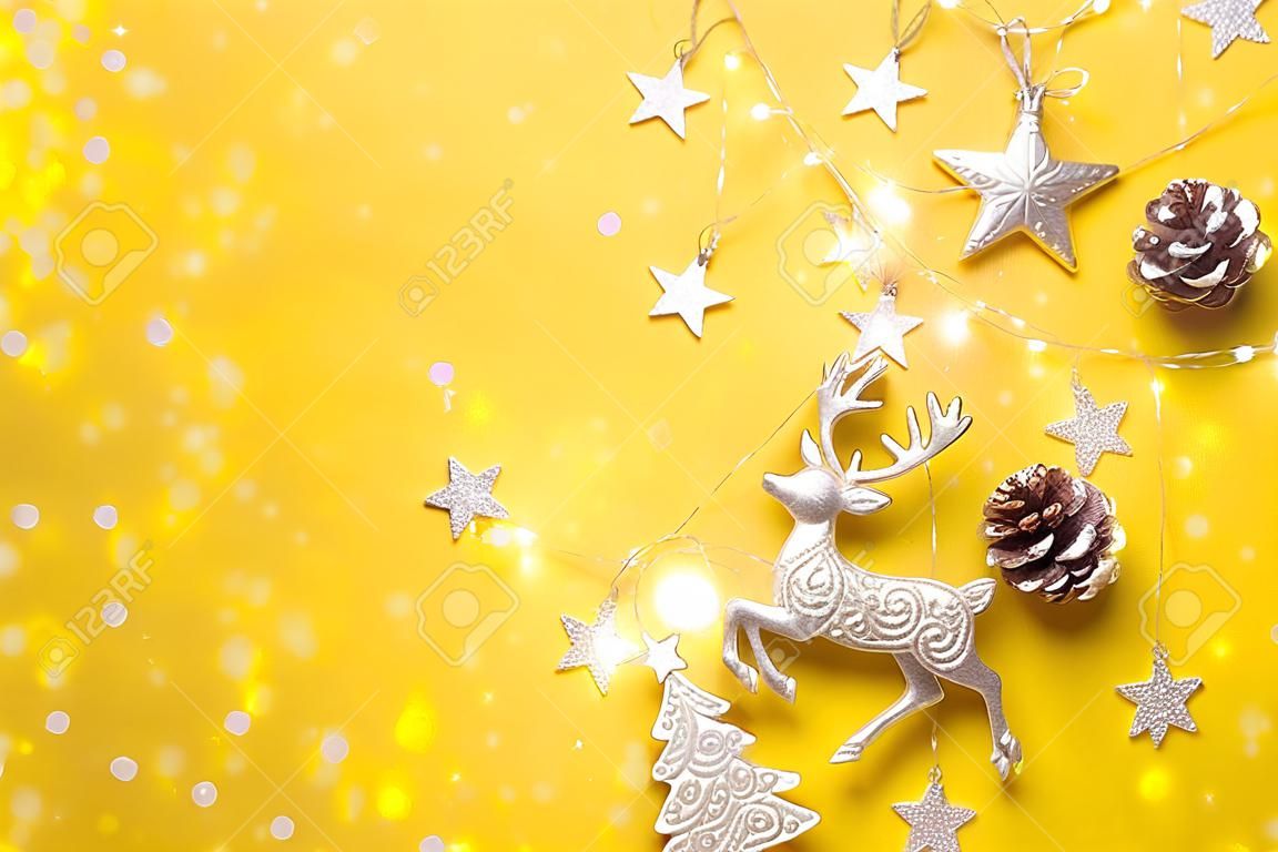 Cervo d'argento lucido, stelle, abete, ghirlanda, bokeh su sfondo giallo.