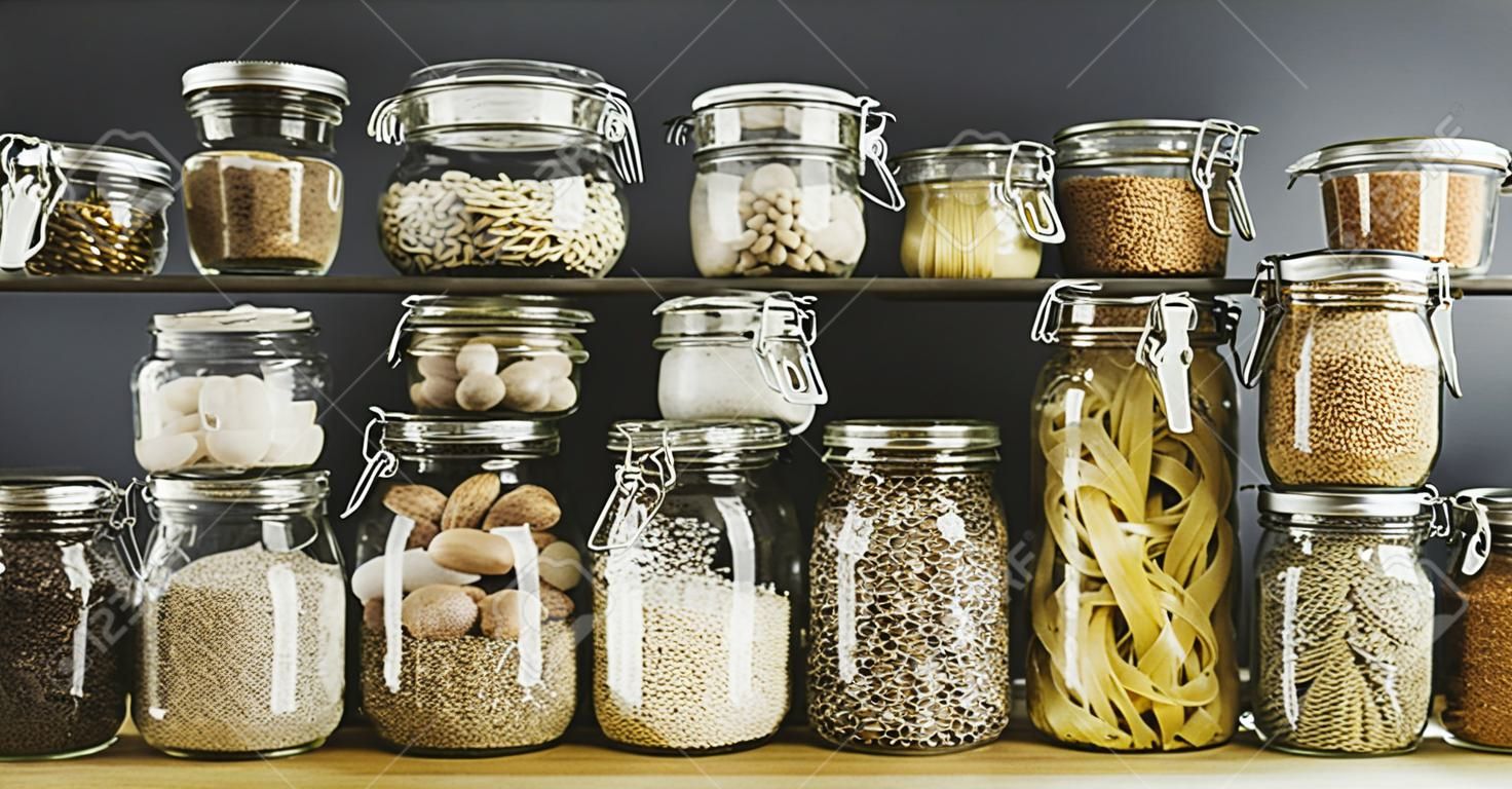 Assortment of uncooked grains, cereals and pasta in glass jars on wooden table. Healthy cooking, clean eating, zero waste concept. Balanced dieting food.