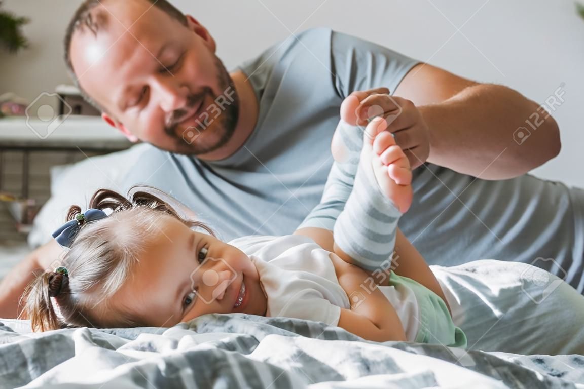 El Padre Juega Con Su Pequeña Hija 2-4 En La Cama. Papá Hace Cosquillas En  Los Pies De Los Niños. Familia, Divirtiéndose Fotos, retratos, imágenes y  fotografía de archivo libres de derecho.